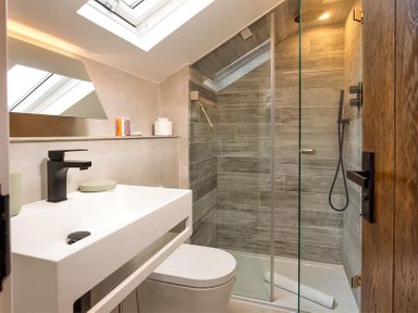A bathroom with a sink, toilet, and glass shower enclosure with tiled walls at Underhowe in Grasmere