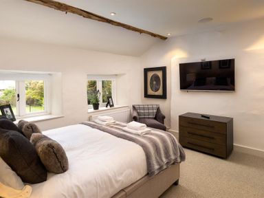 A bedroom with a bed pillows and a blanket a chair a wall mounted tv and windows at Underhowe in Grasmere