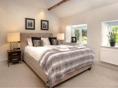 A bedroom with a double bed bedside tables lamps and windows at Underhowe in Grasmere