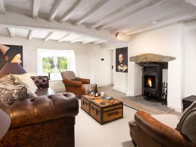 A living room with leather sofas a wooden chest coffee table a wood stove and portraits on walls at Underhowe in Grasmere