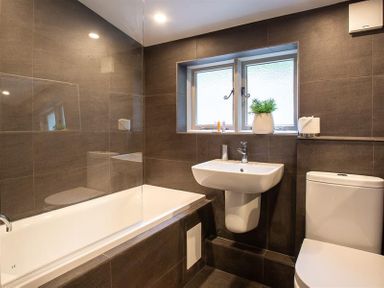 A bathroom with a bathtub a sink a toilet a window with a plant and toiletries at Underhowe in Grasmere