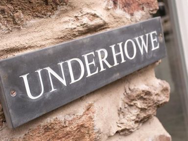 A close up of a metal sign with the word Underhowe on a stone wall at Underhowe in Grasmere