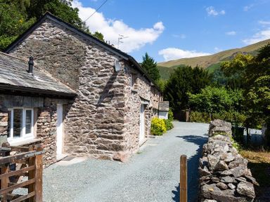 The exterior of a stone house with a gravel driveway and trees surrounding it at Underhowe in Grasmere