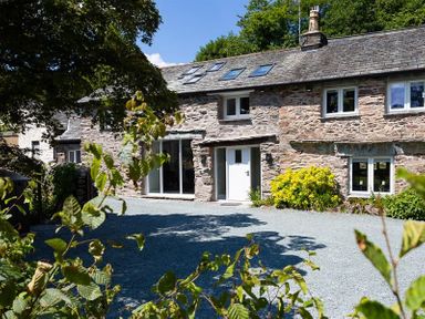 A stone house with white doors and windows surrounded by plants and trees at Underhowe in Grasmere
