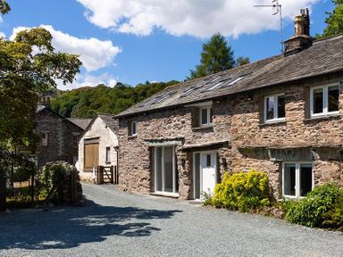 A gravel driveway beside stone cottages with plants and trees at Underhowe in Grasmere