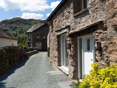 A gravel pathway with stone walls and stone buildings with white doors and windows at Underhowe in Grasmere