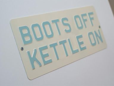 A sign on a wall that reads boots off kettle on