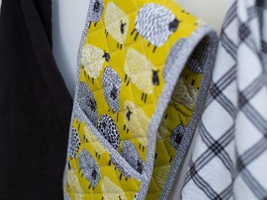 A close-up of a quilted oven mitt with sheep pattern hanging between a black cloth and a white and black checkered cloth at Hill Cottage in Ambleside