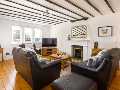 A living room with black leather sofas a wooden coffee table a television and a fireplace at Hill Cottage in Ambleside