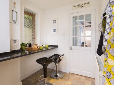 A small kitchen area with two black bar stools and a countertop with cups and a tray at Hill Cottage in Ambleside