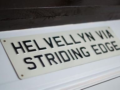 A sign with the text helvellyn via striding edge mounted on a white surface