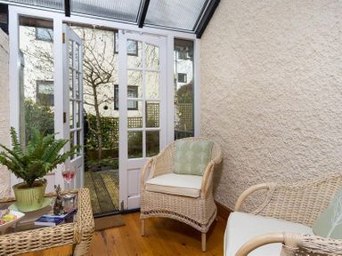 A conservatory with wicker chairs a table and glass doors leading to a garden at Hill Cottage in Ambleside