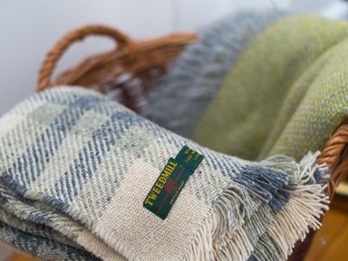 A woven basket containing folded plaid blankets with a Tweedmill label at Hill Cottage in Ambleside