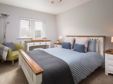 A bedroom with a bed with striped bedding two bedside tables a dressing table an armchair and a floor lamp at Hill Cottage in Ambleside