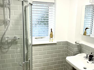A bathroom with a corner shower unit a window with blinds a sink and a mirror at Hill Cottage in Ambleside