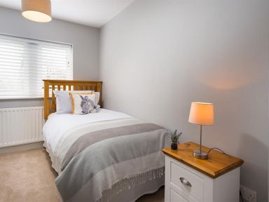 A bedroom with a single wooden bed white bedding a rabbit pillow a bedside table with a lamp and a small plant at Hill Cottage in Ambleside