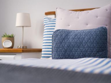 A bed with three pillows and a bedside table with a lamp plant and clock at Hill Cottage in Ambleside