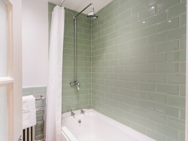 A bathtub with a showerhead and green tiled walls in a bathroom at Hill Cottage in Ambleside