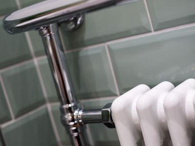 A close up of chrome plumbing pipes and a white radiator against green tiled wall at Hill Cottage in Ambleside