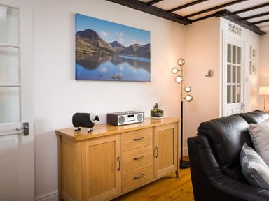 A wooden cabinet with a radio speaker a black and white sheep figurine and a small plant next to a black leather sofa in a living room at Hill Cottage in Ambleside