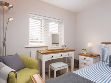 A bedroom with a green armchair a white dressing table with a stool and a bed with striped bedding at Hill Cottage in Ambleside