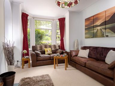 A living room with brown leather sofas red curtains wooden tables and a three-panel wall art at Ellerthwaite House in Windermere