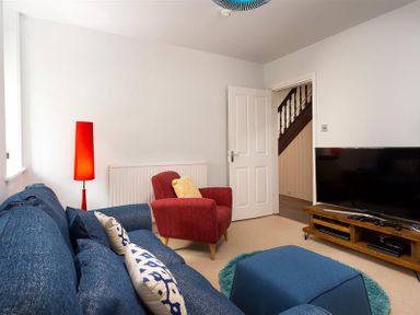 A living room with a blue sofa and ottoman a red armchair a red floor lamp and a television on a wooden stand at Ellerthwaite House in Windermere