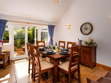 A dining room with wooden table and chairs set for a meal next to glass doors leading to a garden at Ellerthwaite House in Windermere