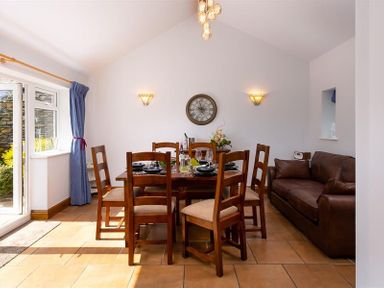 A dining room with wooden table and chairs beside a brown leather sofa at Ellerthwaite House in Windermere