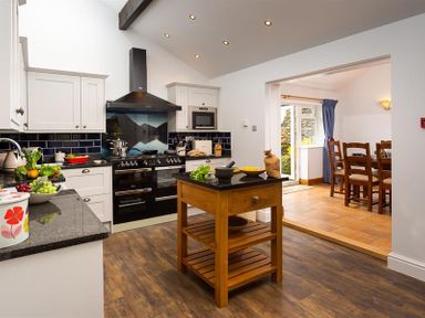 A kitchen with white cabinets black appliances a wooden island and a dining area visible through an open doorway at Ellerthwaite House in Windermere