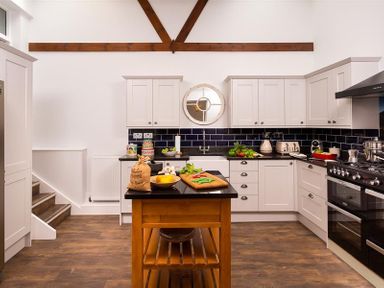 A kitchen with white cabinets a wooden island and black countertops at Ellerthwaite House in Windermere