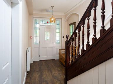 A hallway with a wooden staircase a bench a door with stained glass panels and a hanging light at Ellerthwaite House in Windermere