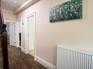 A hallway with wooden floor multiple doorways a staircase and a wall painting at Ellerthwaite House in Windermere