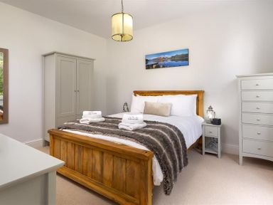 A bedroom with a wooden bed frame a wardrobe a chest of drawers and a nightstand at Ellerthwaite House in Windermere