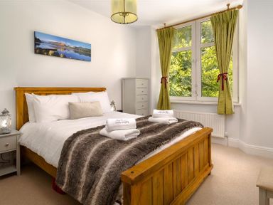 A bedroom with a wooden bed frame green curtains and a chest of drawers at Ellerthwaite House in Windermere