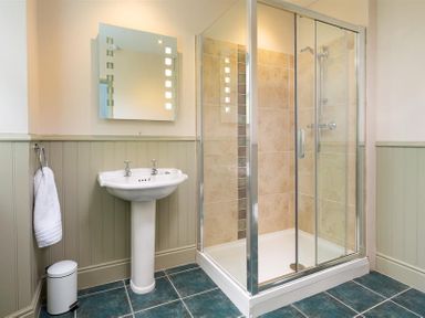 A bathroom with a pedestal sink a mirror a towel hanging on a ring and a glass shower enclosure at Ellerthwaite House in Windermere