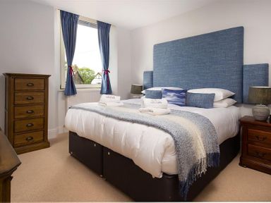 A bedroom with a bed featuring blue headboard and pillows beside wooden dressers at Ellerthwaite House in Windermere