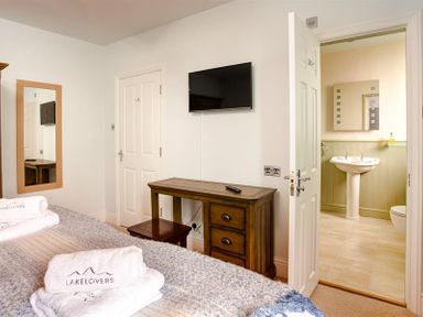 A bedroom with a bed towels on it a wall mirror a wooden dressing table and an open door leading to a bathroom at Ellerthwaite House in Windermere