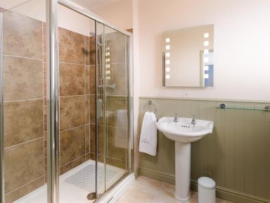 A bathroom with a glass shower enclosure a pedestal sink and a wall mirror at Ellerthwaite House in Windermere