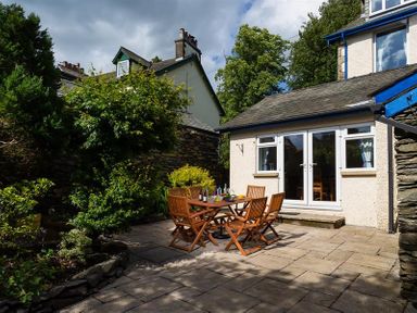 An outdoor patio area with wooden table and chairs and plants around at Ellerthwaite House in Windermere