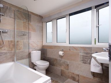 A bathroom with a bathtub shower combination toilet sink and frosted windows at Ellerthwaite House in Windermere