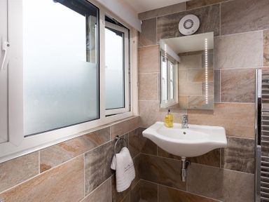A bathroom with a wall-mounted sink mirror towel holder and frosted window at Ellerthwaite House in Windermere