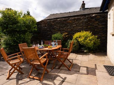 A patio with wooden chairs and a table with drinks and fruit in a garden at Ellerthwaite House in Windermere
