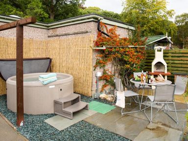 An outdoor patio area with a hot tub towels table with chairs bottles and bread near a barbecue at Heathfield in Keswick