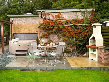 An outdoor patio with a round table and four chairs a hot tub with towels and a chimney barbecue at Heathfield in Keswick