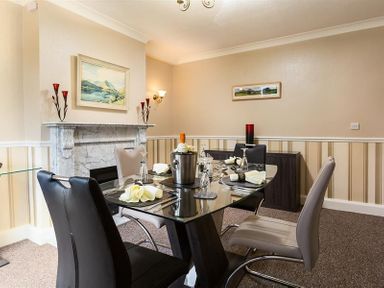 A dining room with a glass table set for four and a marble fireplace in the background at Heathfield in Keswick