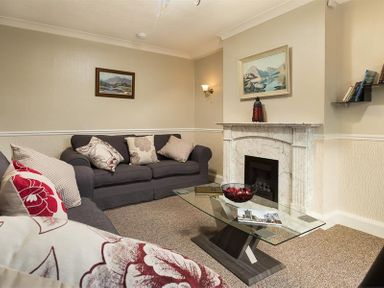 A living room with two sofas a glass coffee table a fireplace and paintings on the wall at Heathfield in Keswick