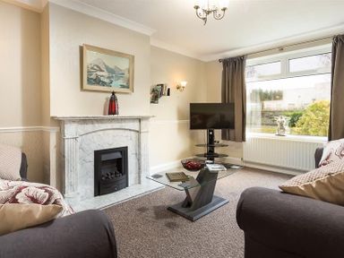 A living room with a marble fireplace a glass coffee table a television and a large window at Heathfield in Keswick