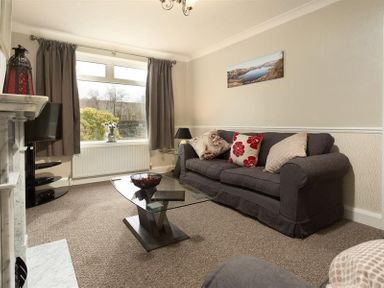 A living room with a dark sofa and cushions a glass coffee table a television and curtains at Heathfield in Keswick