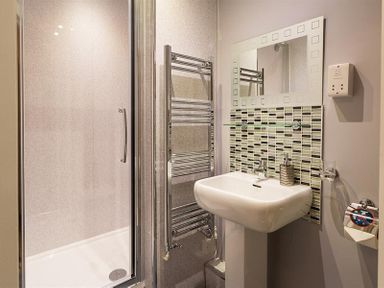 A bathroom with a shower enclosure a towel rail a pedestal sink and a mirror above the sink at Heathfield in Keswick